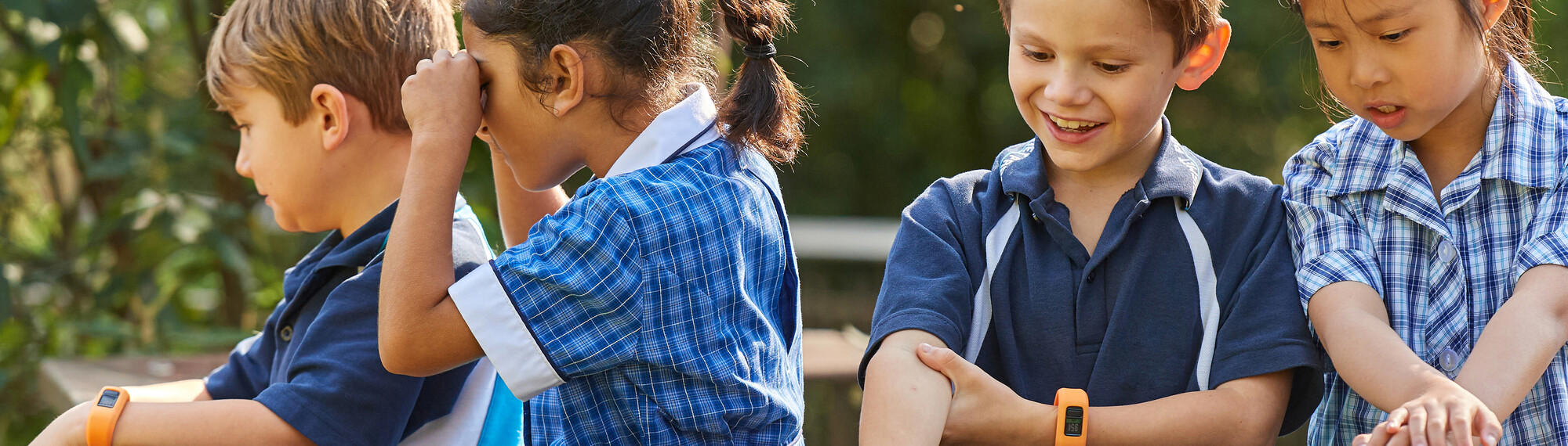 A group of young young primary school aged children sit and play dressed in blue uniforms