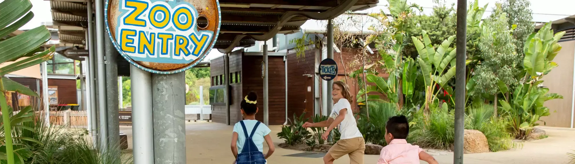 Three kids running past a sign that says Zoo Entry