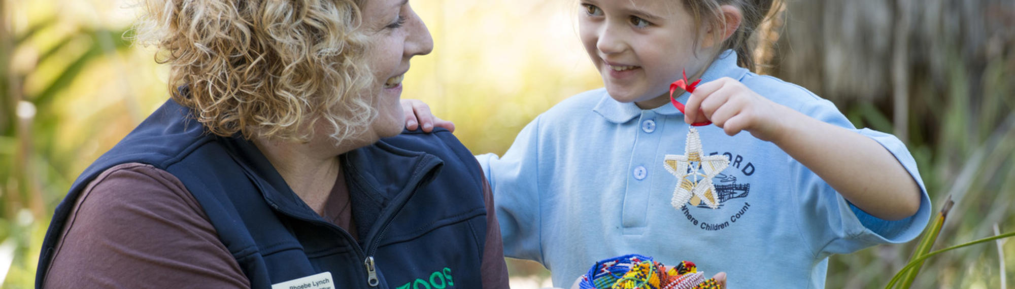 Student with Educator holding up a beads for wildlife craft creation