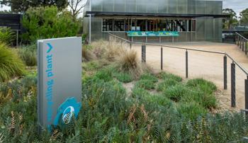 Sign reading 'recycling plant' in a garden bed pointing towards a building