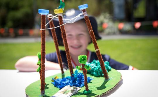 A boy wearing a hat sits behind a crafted replica of an exhibit