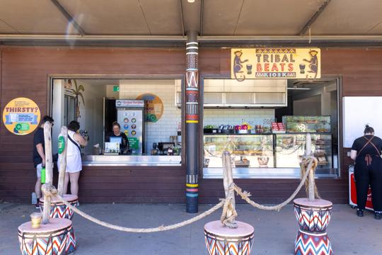 A kiosk-style building with two people waiting in line to be served. The building says Tribal Beats Kiosk on it.