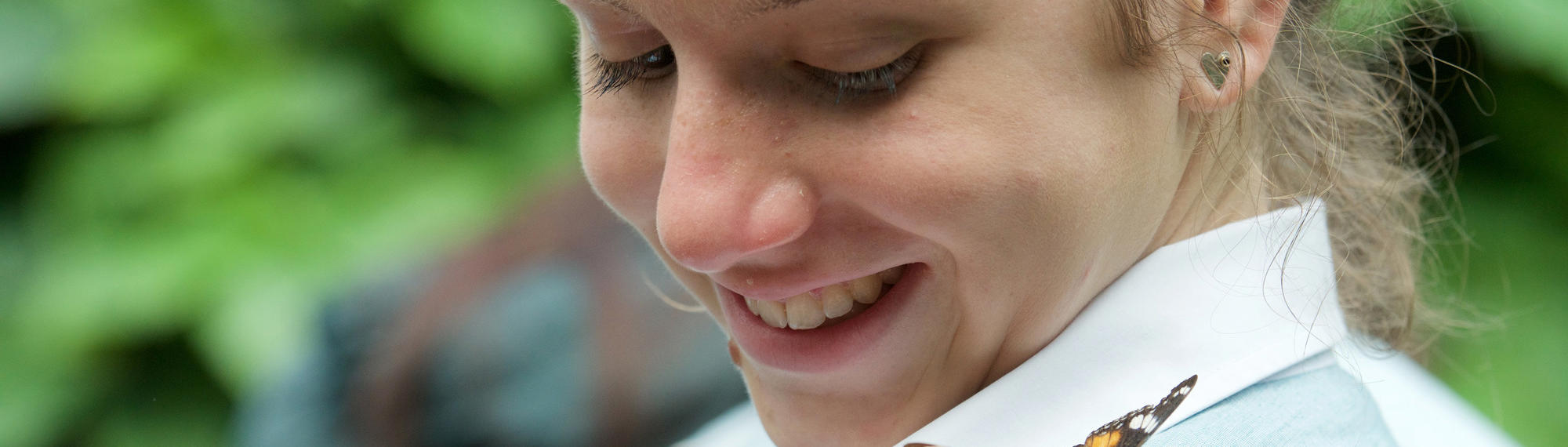 A secondary student smiles as she looks at a butterfly on her shoulder.