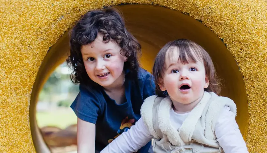 Two children crawling in a yellow tunnel, looking at the camera.