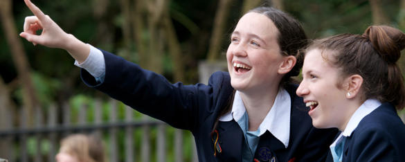 Two students smile as one points into the air