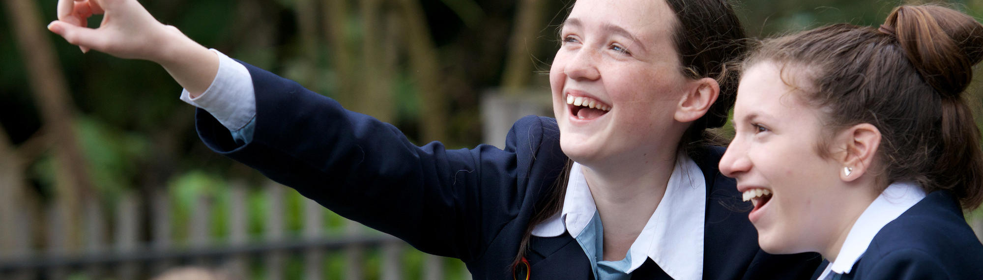 Two students smile as one points into the air