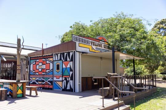 A building with colourful artwork painted on the side. The building says Village Kitchen on the front of it.